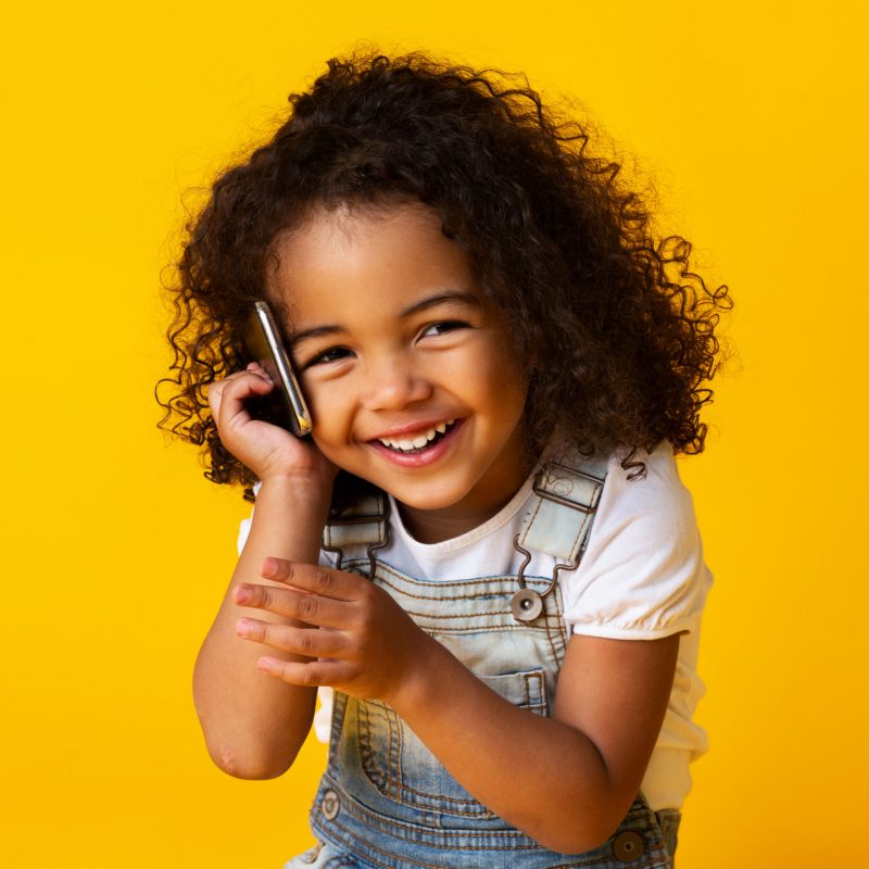 Cute afro girl talking on cellphone and smiling on yellow studio background